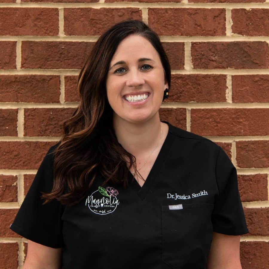 Dr. Jessica smith in black magnolia family dental scrubs standing in front of a brick wall.