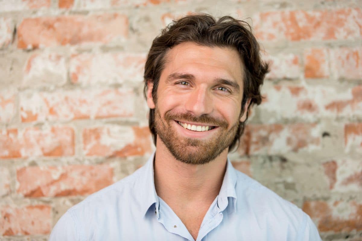 Smiling adult man with straight, healthy teeth standing against a brick background