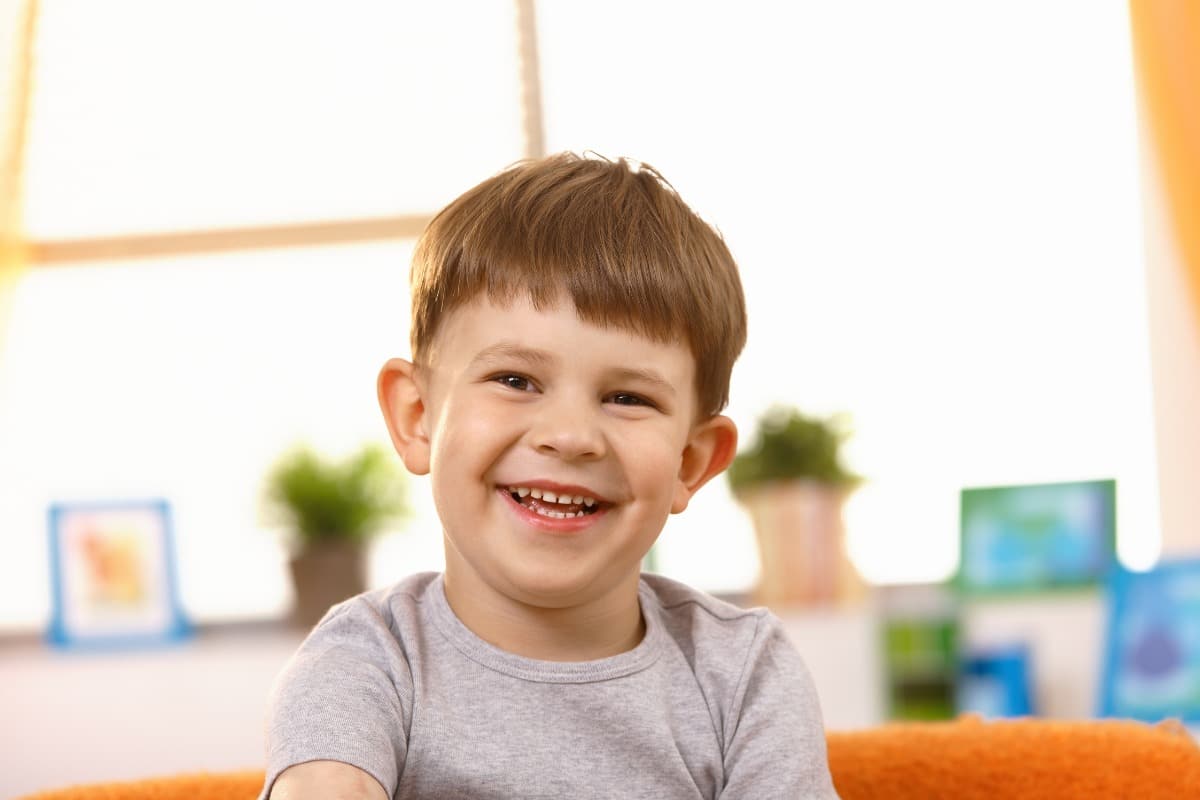 Smiling young boy sitting indoors with a bright, happy expression.