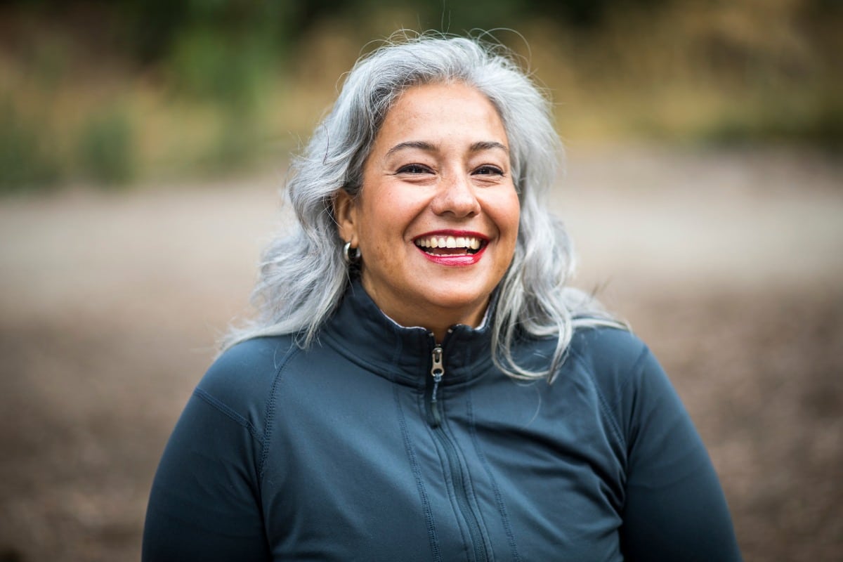 Smiling woman with gray hair standing outdoors, expressing confidence and happiness.