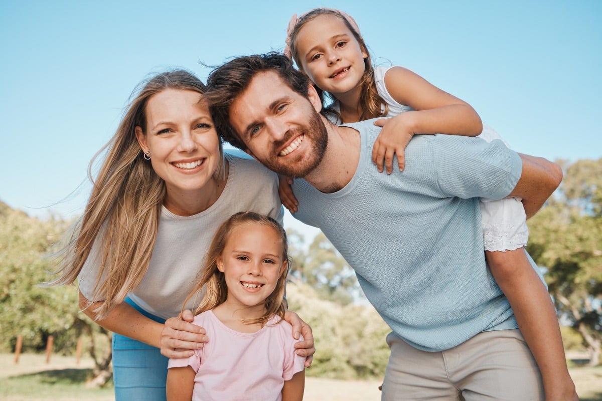Happy family of four smiling outdoors on a sunny day.