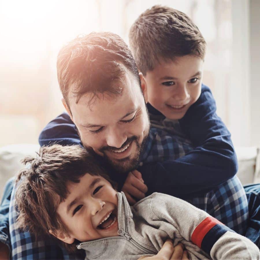 Father laughing and cuddling with his two young sons at home.