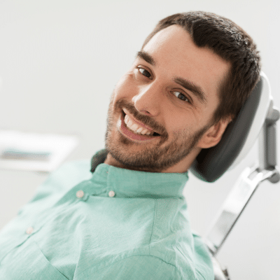 Young man sitting in a dental chair smiling, representing restorative dental treatment