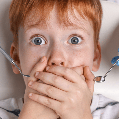 Little boy with his hands over his mouth with eyes wide, representing dental anxiety in children